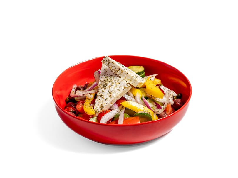 Vibrant Greek salad with feta, tomatoes, cucumbers, olives, and onions in a red bowl.