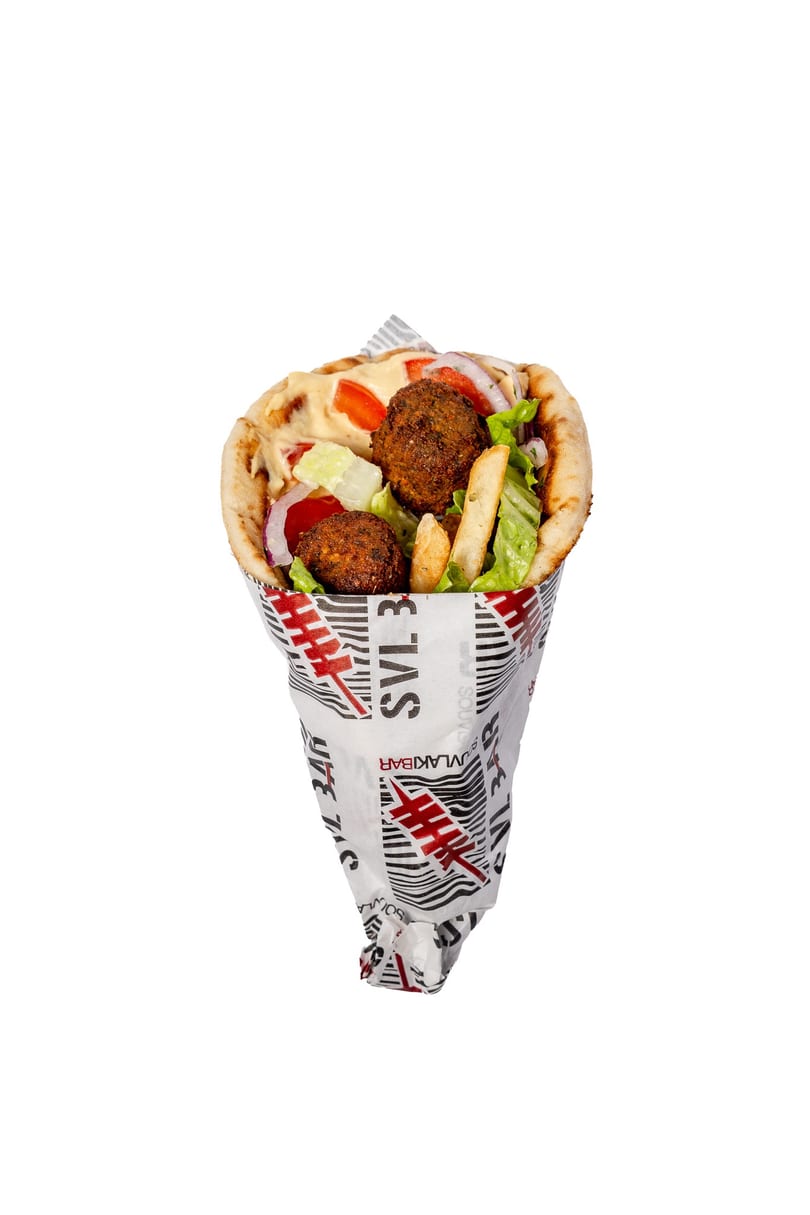 Falafel pita wrap with lettuce, tomatoes, onions, fries, and sauce, wrapped in branded paper.