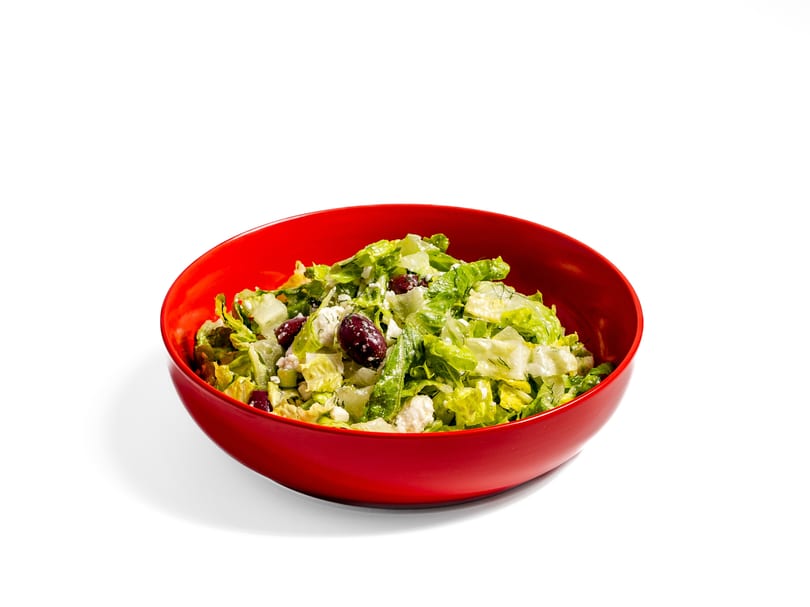 A vibrant red bowl filled with a fresh green salad, feta cheese, and dark olives.