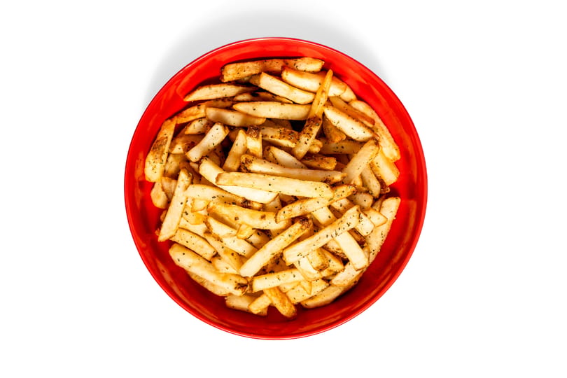 Overhead view of a red bowl filled with golden french fries seasoned with herbs and pepper.